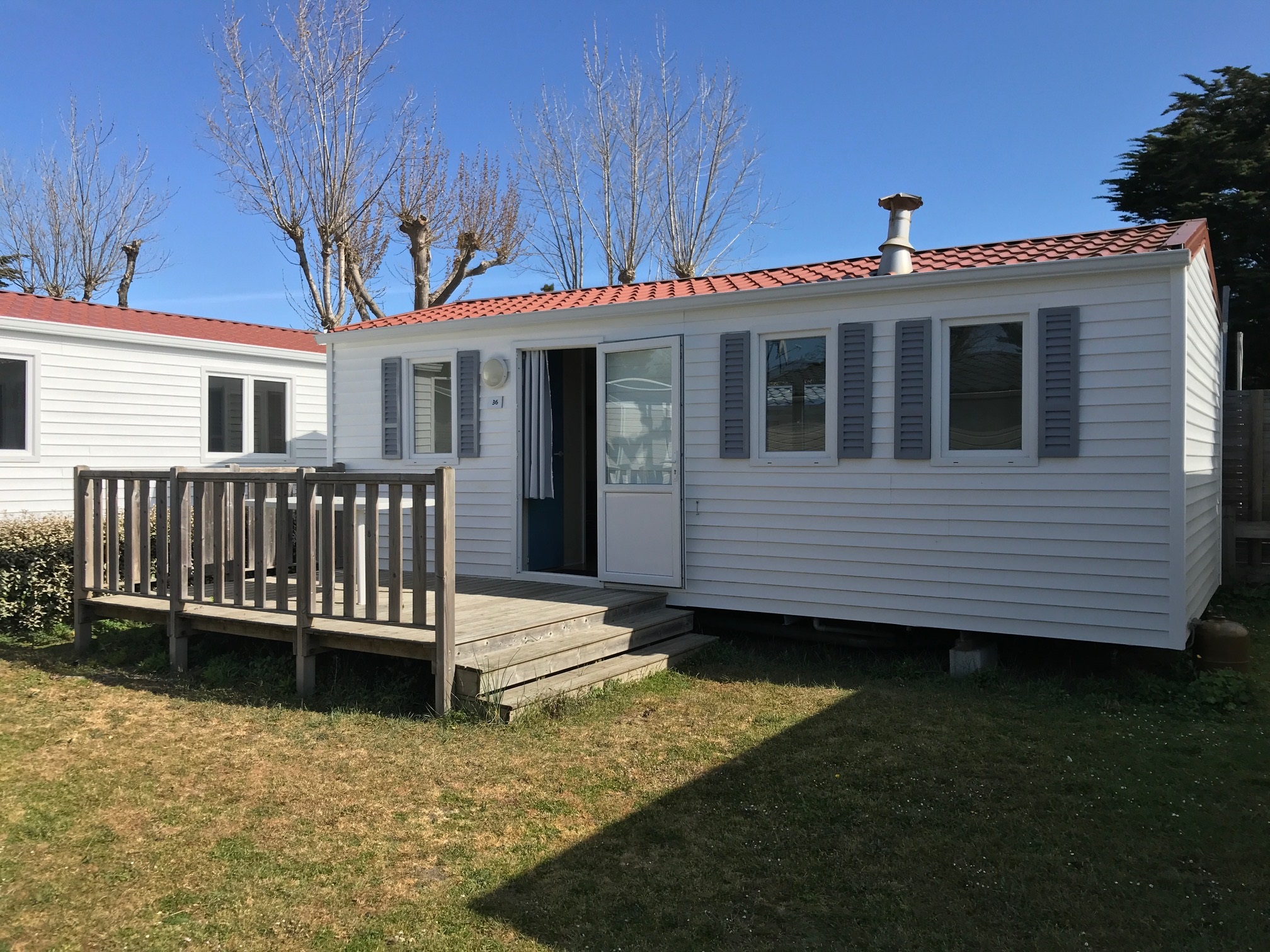 Mobil-home blanc avec terrasse en bois.