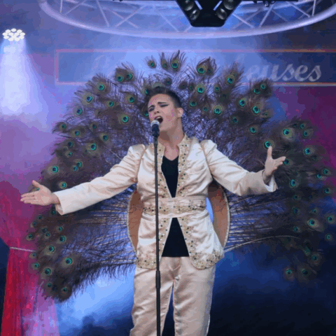 Singer in costume with peacock feathers on stage.